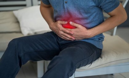 a person in a blue shirt clutches their abdomen which is highlighted with a red light